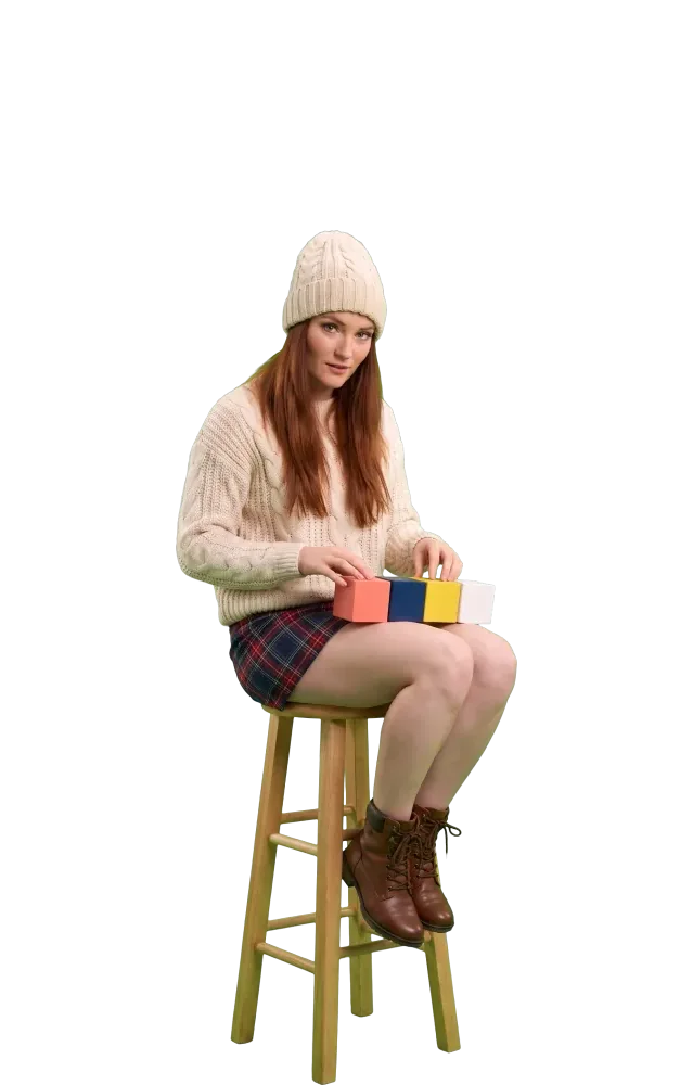 Woman on a stool arranging four coloured blocks